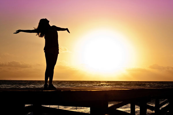Person mit ausgebreiteten Armen vor einem Sonnenuntergang