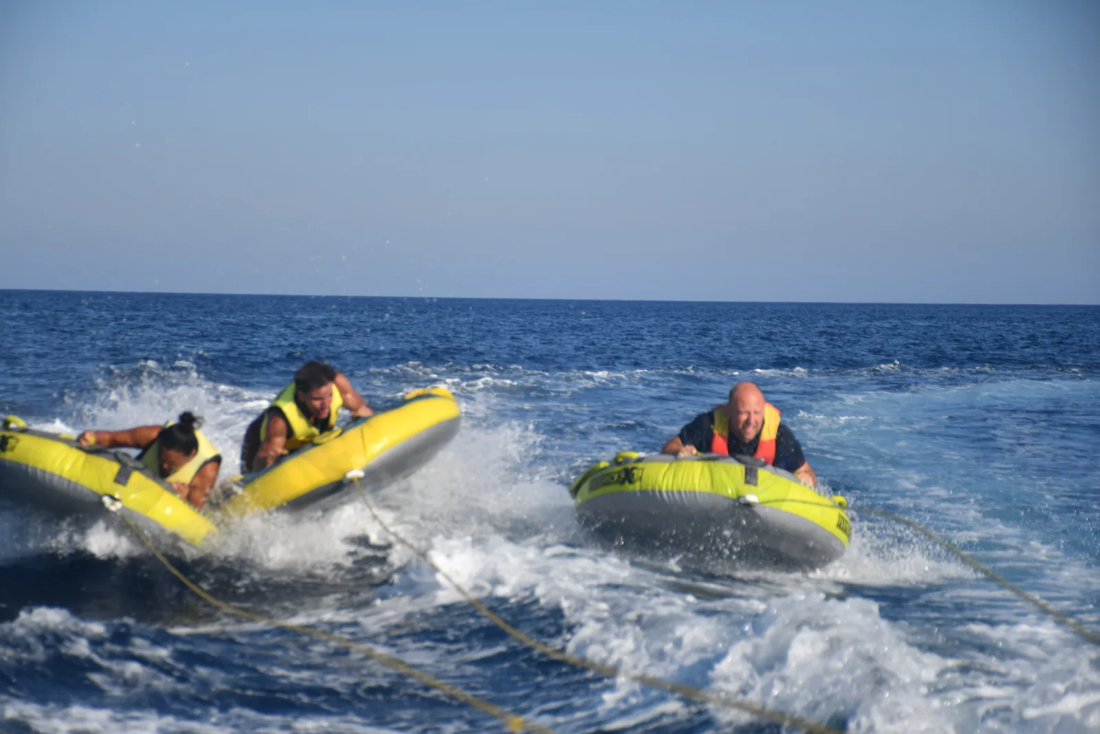 Gemeinsamer Wassersport: Drei Personen werden auf aufblasbaren Reifen von einem Boot über das Meer gezogen