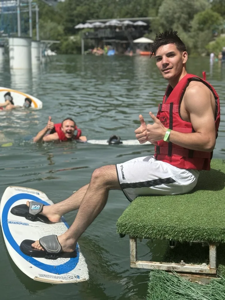 Ein Teilnehmer beim Wakeboarden, ein weiterer winkt aus dem Wasser