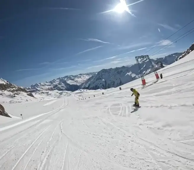 Snowboard-Abfahrt auf einer sonnigen Piste vor verschneitem Bergpanorama